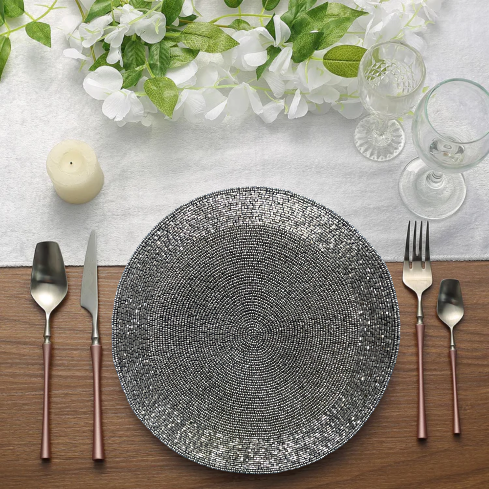 Decorative plate with silverware on a wooden table with flowers and candles in the background